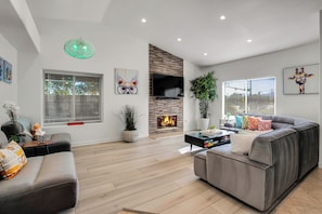 A modern living room with a fireplace, grey sofas, and a flat-screen TV. - Flora Vista Sunshine (Palm Springs)
