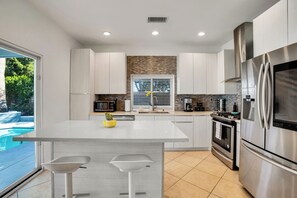 A modern kitchen with a central island, stainless steel appliances, and a view of a swimming pool. - Flora Vista Sunshine (Palm Springs)