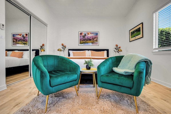 A bedroom with a bed, two green armchairs, a small table with a plant, and two framed pictures on the wall. - Flora Vista Sunshine (Palm Springs)