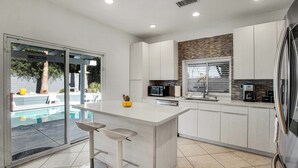 A modern kitchen with a central island, a built-in microwave, and a refrigerator. - Flora Vista Sunshine (Palm Springs)