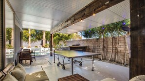 An outdoor patio area with a ping pong table, cushioned seating, and a barbecue grill. - Flora Vista Sunshine (Palm Springs)