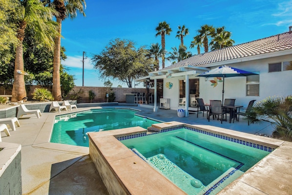 A swimming pool with a tiled deck, lounge chairs, and a patio area with tables and chairs. - Flora Vista Sunshine (Palm Springs)