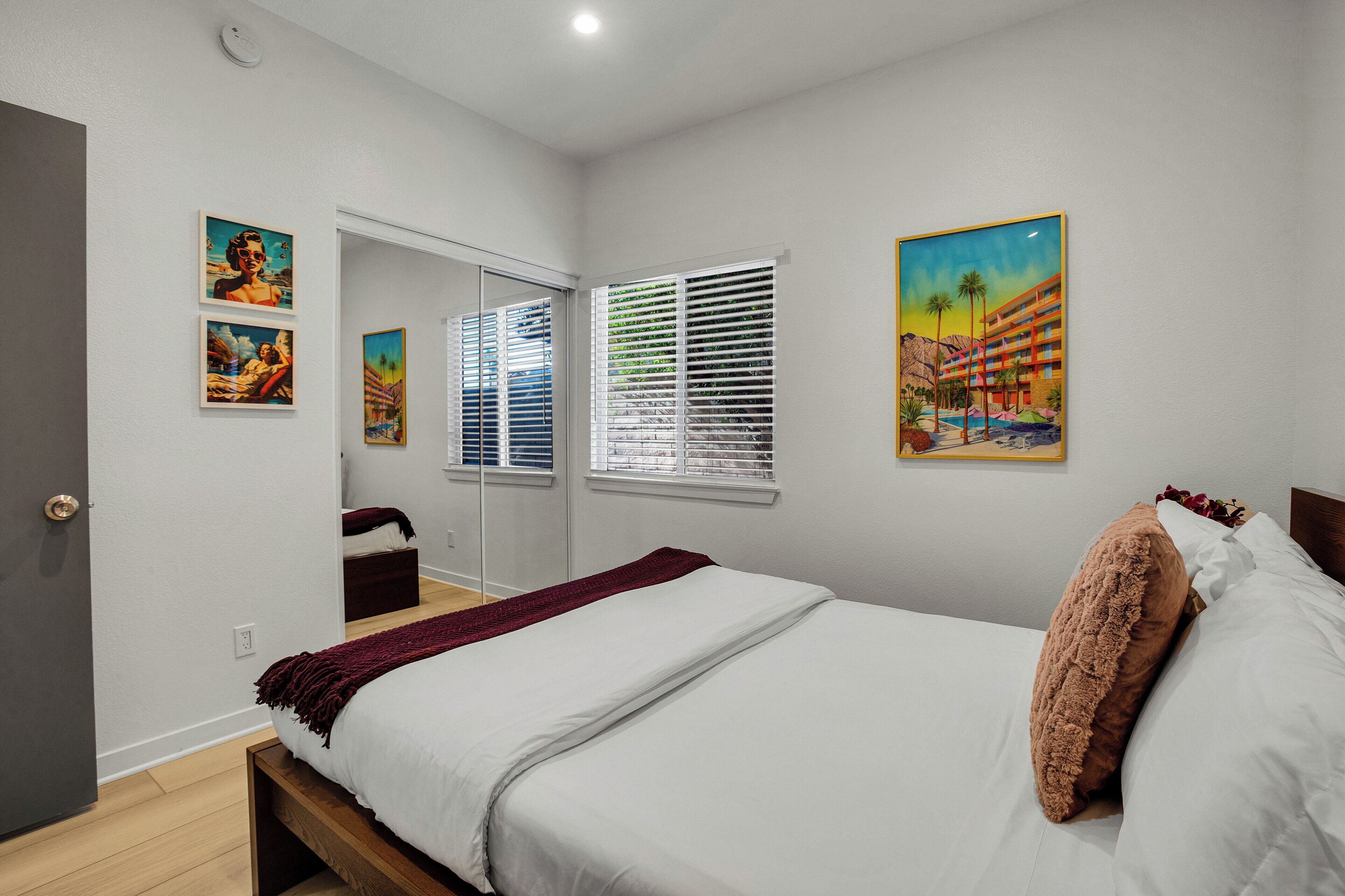 A bedroom with a bed, a window with blinds, and a painting on the wall.