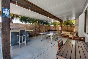 Une terrasse extérieure avec une table, des chaises, un canapé et un panneau indiquant un espace barbecue.
