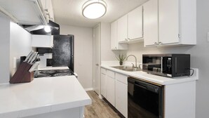 A compact kitchen with white cabinetry, a stove, a microwave, and a dishwasher.