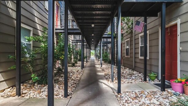 A covered walkway with a metal roof, flanked by buildings with windows and doors, and a small American flag.