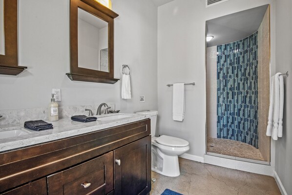 A bathroom with a marble sink, dark wooden vanity, white toilet, and a shower with blue mosaic tiles.