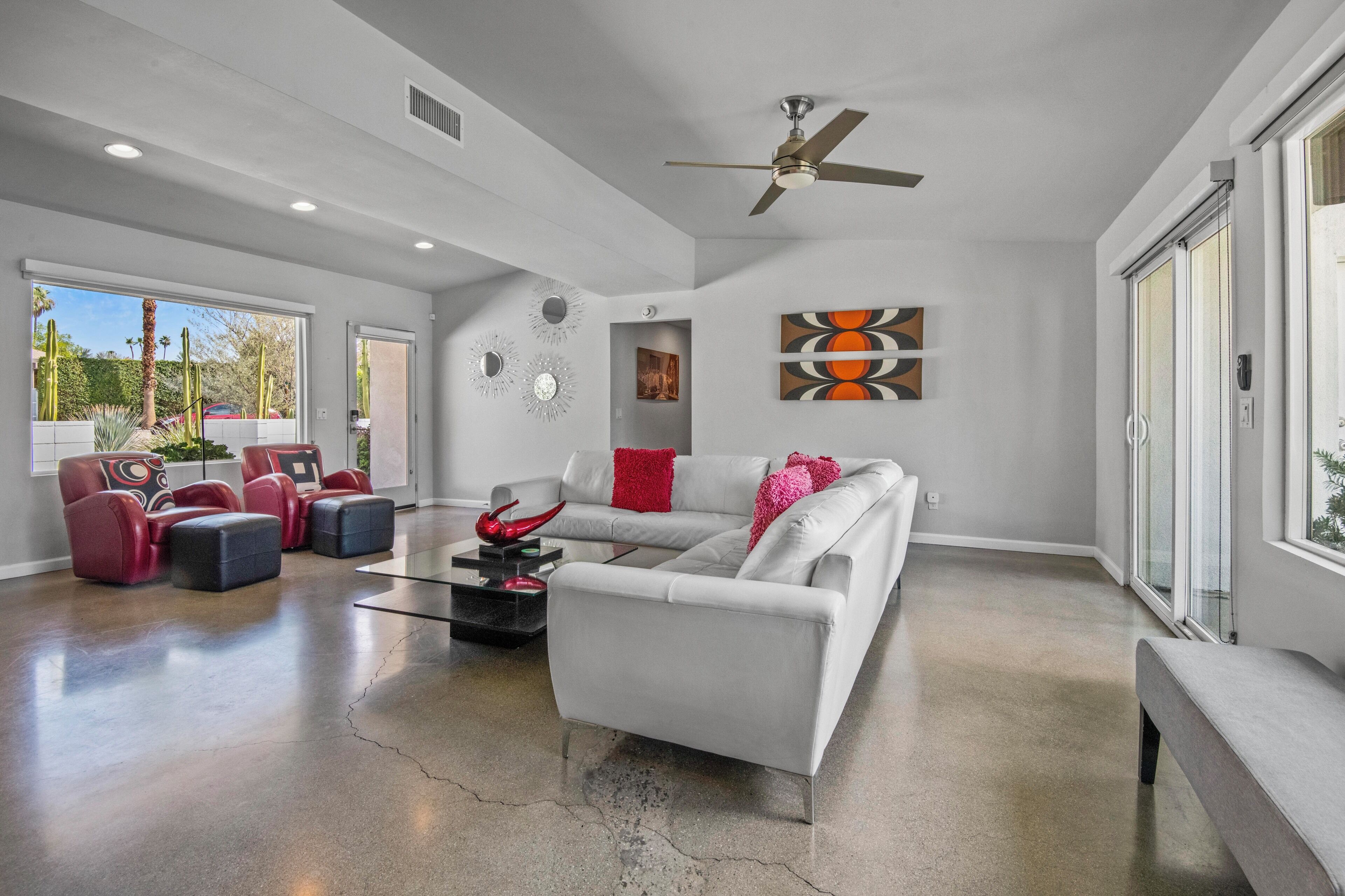 A spacious living room with a white sofa, red and black chairs, a coffee table, and a ceiling fan.