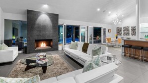 Una sala de estar moderna con chimenea, sofás blancos, una mesa de centro y una zona de bar.