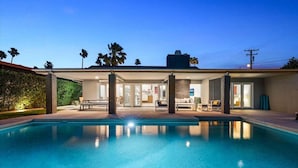 Una casa moderna con piscina, mobiliario exterior y palmeras.