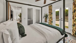 Een hemelbed met witte lakens, een plafondventilator en uitzicht buiten via glazen deuren.