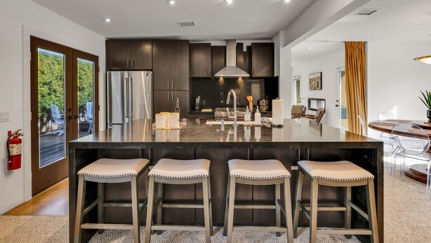 Een moderne keuken met een groot kookeiland, roestvrijstalen apparatuur en barstoelen.