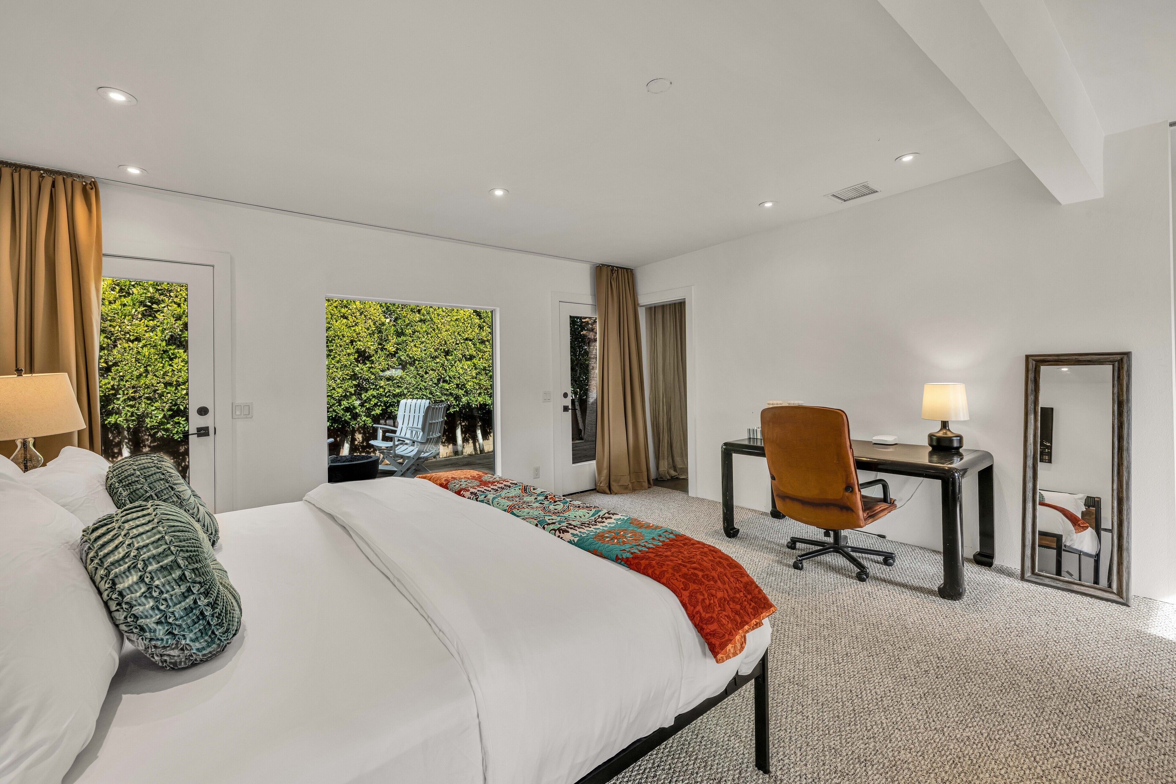 A hotel room with a large bed, a desk, a chair, and a view of greenery outside.