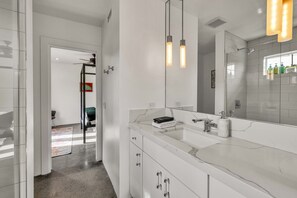 A modern bathroom with a large mirror, white marble countertop, and a shower area. - Mid-Century Elegance & Fun in Tahquitz River Estates (Palm Springs)