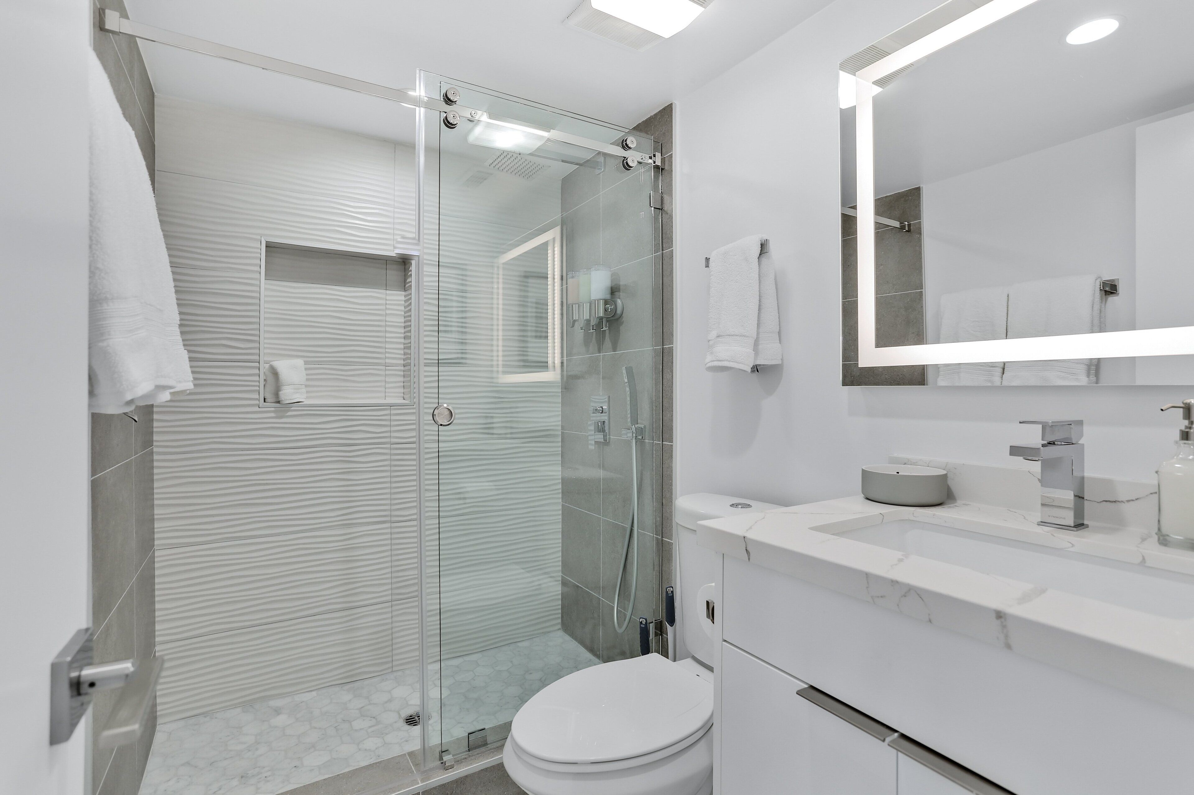 A modern bathroom with a glass-enclosed shower, a white sink, and a large mirror.