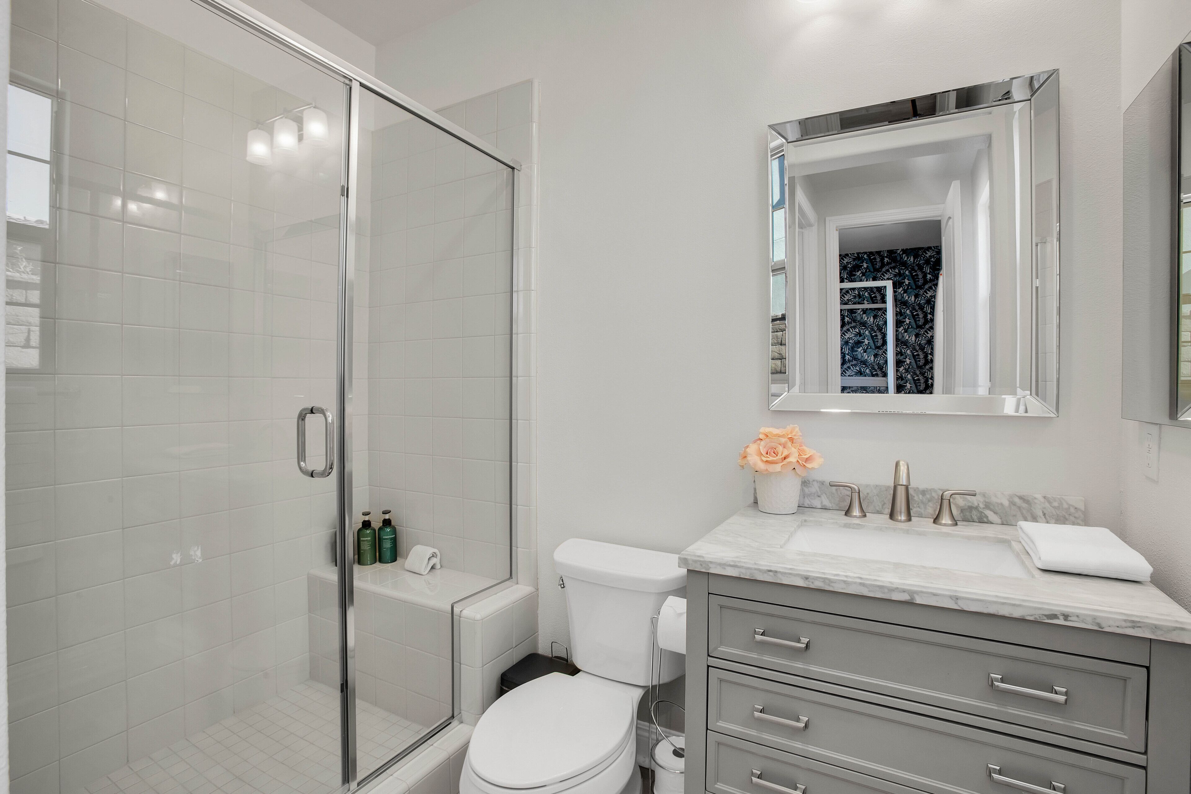 A modern bathroom with a glass shower enclosure, a white toilet, and a marble countertop with a sink and mirror.