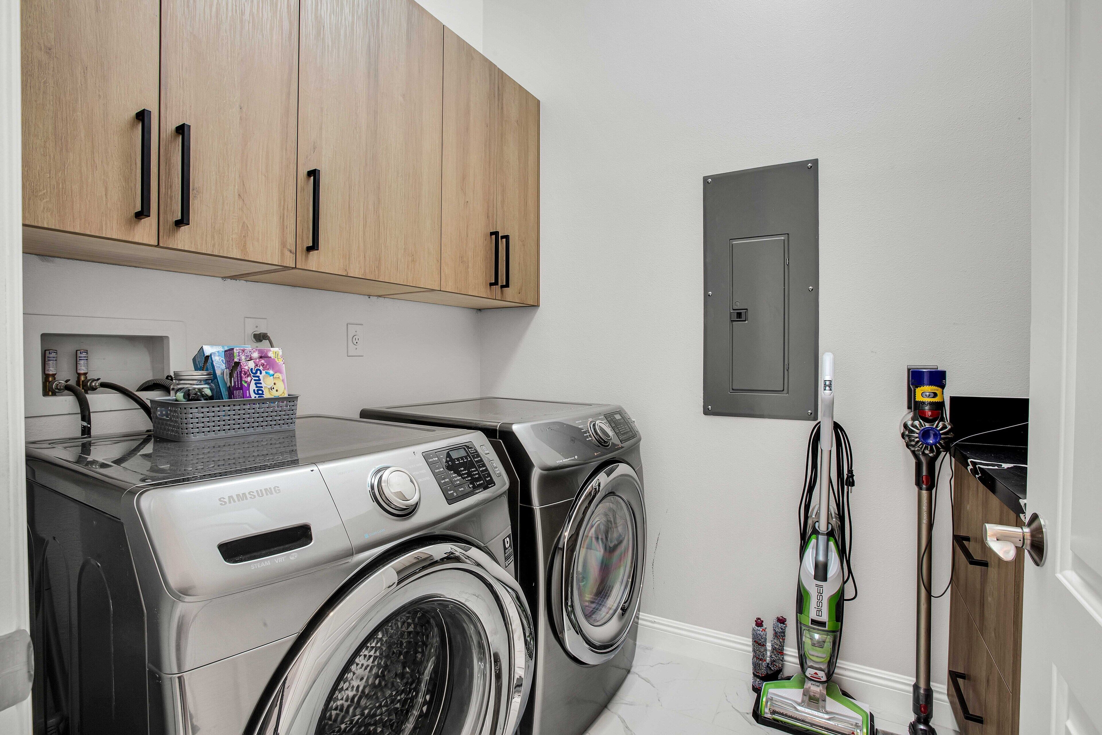 A laundry area with two washing machines, a vacuum cleaner, and wooden cabinets.