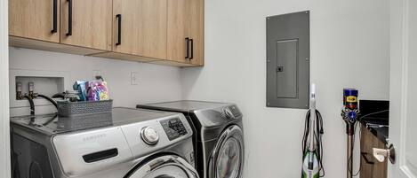 A laundry area with two washing machines, a vacuum cleaner, and wooden cabinets.