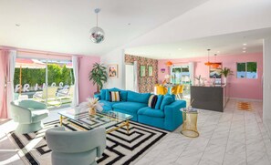 A spacious living area with a blue sofa, a glass coffee table, and a modern kitchen in the background. - Caliente Oasis (Palm Springs)