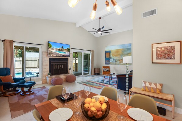A spacious living room with a fireplace, a dining area with a table set for four, and a large TV screen. - Stylish Boho Treasure (Palm Springs)