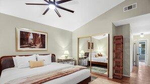 Ein Hotelzimmer mit einem großen Bett, Nachttischen, einem Deckenventilator, einem Spiegel und Blick auf den Flur.