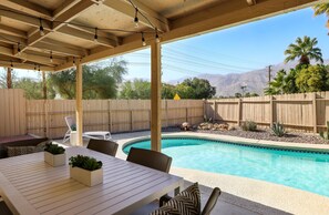 A covered outdoor area with a pool, seating, and a wooden fence. - Stylish Boho Treasure (Palm Springs)
