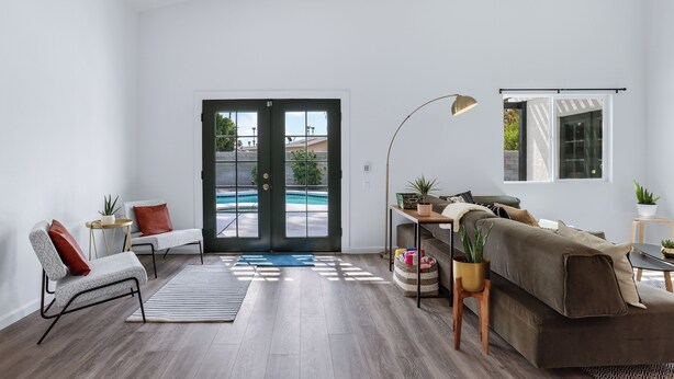 A modern living room with a pool view, a sofa, a coffee table, and a desk with a lamp. - Desert Green Serenity (Palm Springs)