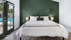 A bedroom with a green accent wall, a large bed with white bedding, and a view of a pool through a glass door. - Desert Green Serenity (Palm Springs)