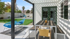 An outdoor patio with a table and chairs, a pergola, and a view of a mountain range. - Desert Green Serenity (Palm Springs)