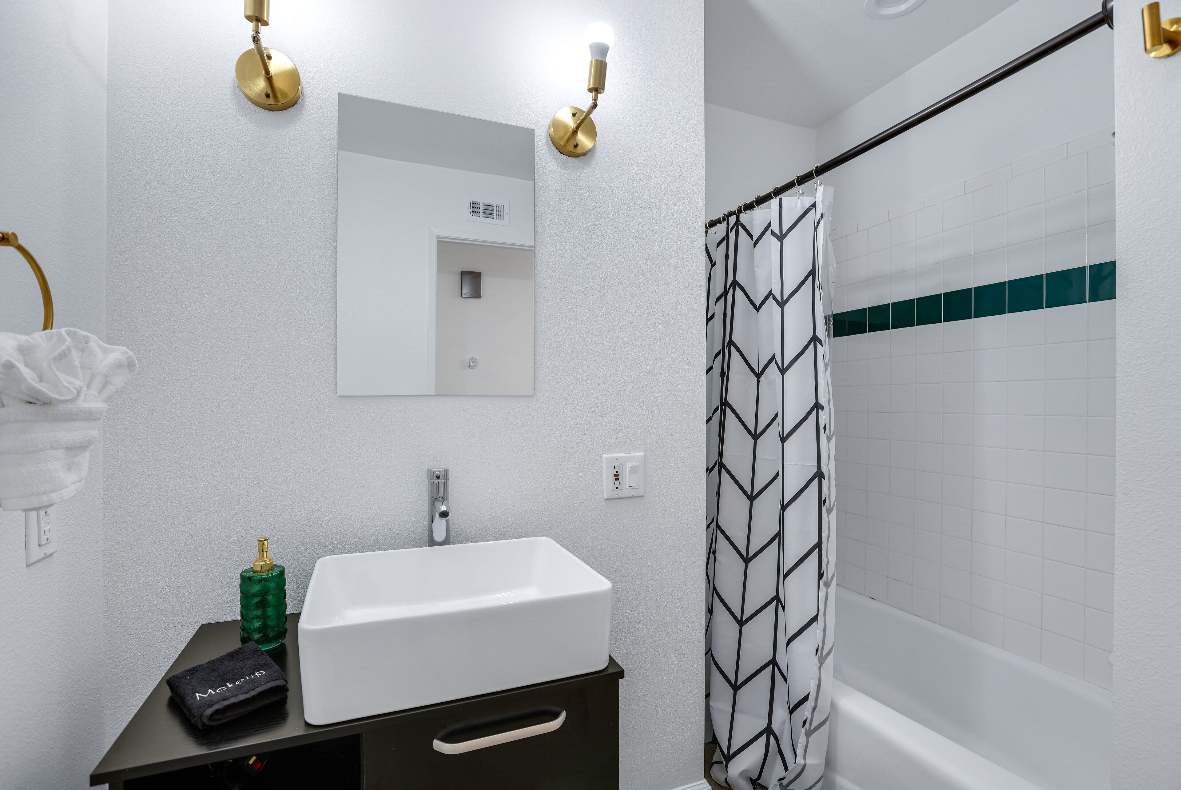 Un baño con lavamanos blanco, espejo, toalla y cortina de ducha.