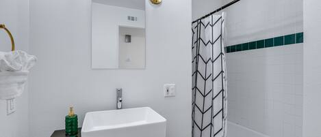 Un baño con lavamanos blanco, espejo, toalla y cortina de ducha.