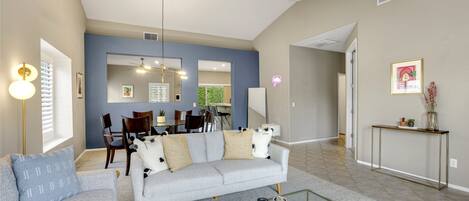 A modern living room with a grey sofa, coffee table, and dining area in the background.