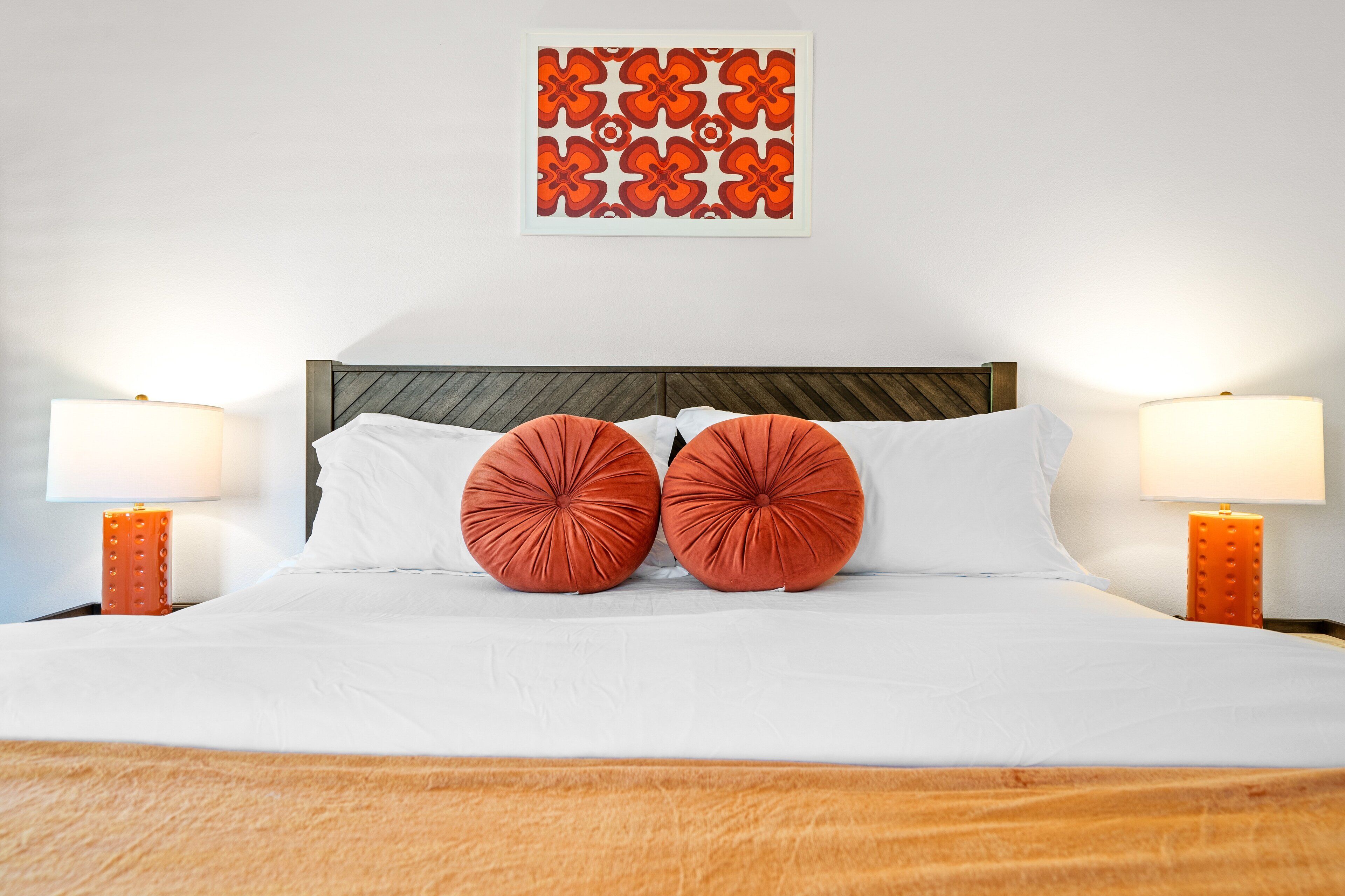 Una cama bien hecha con sábanas blancas, dos almohadas rojas y un cabecero de madera.