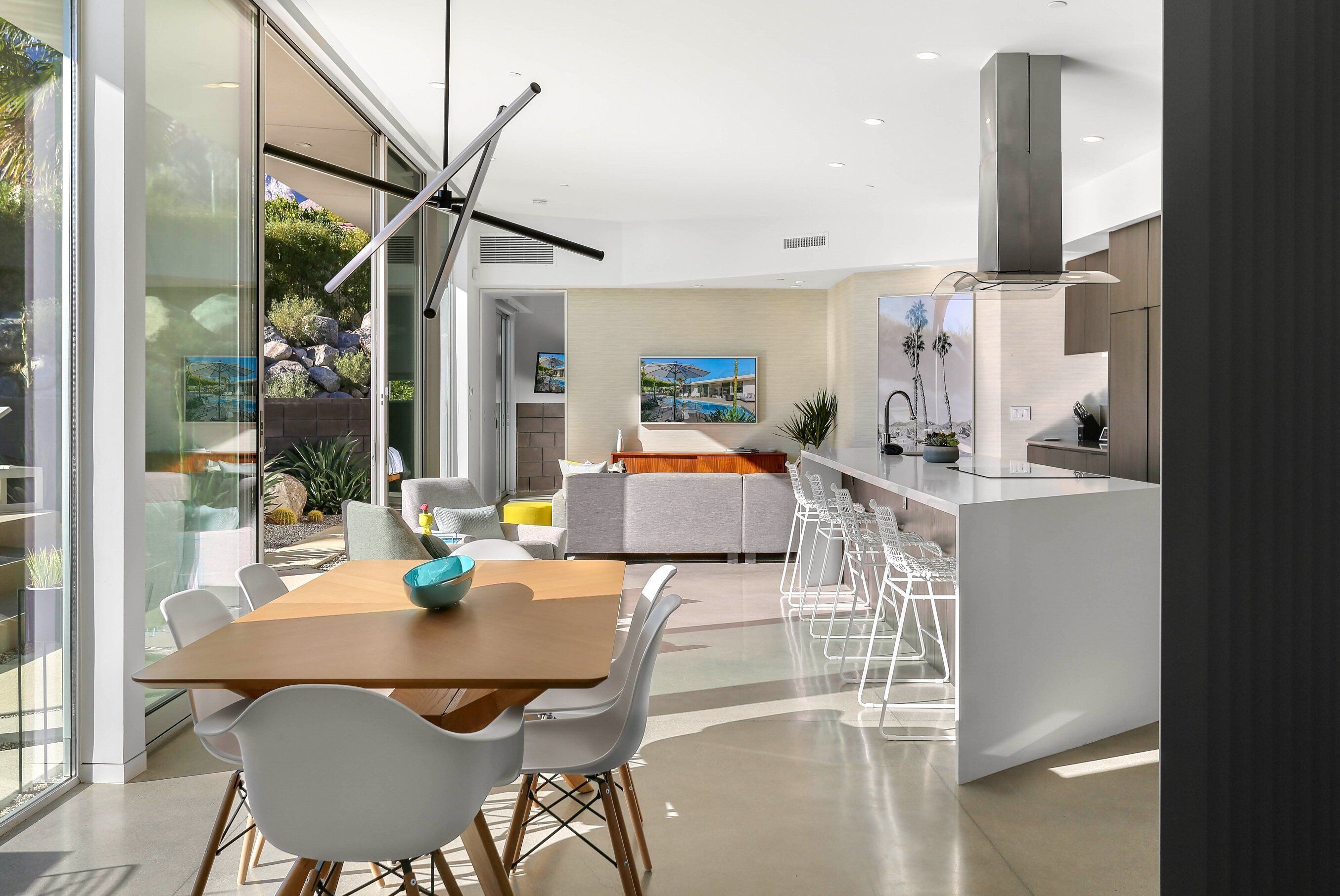 A modern kitchen with a dining area, large windows, and a view of the outdoors.