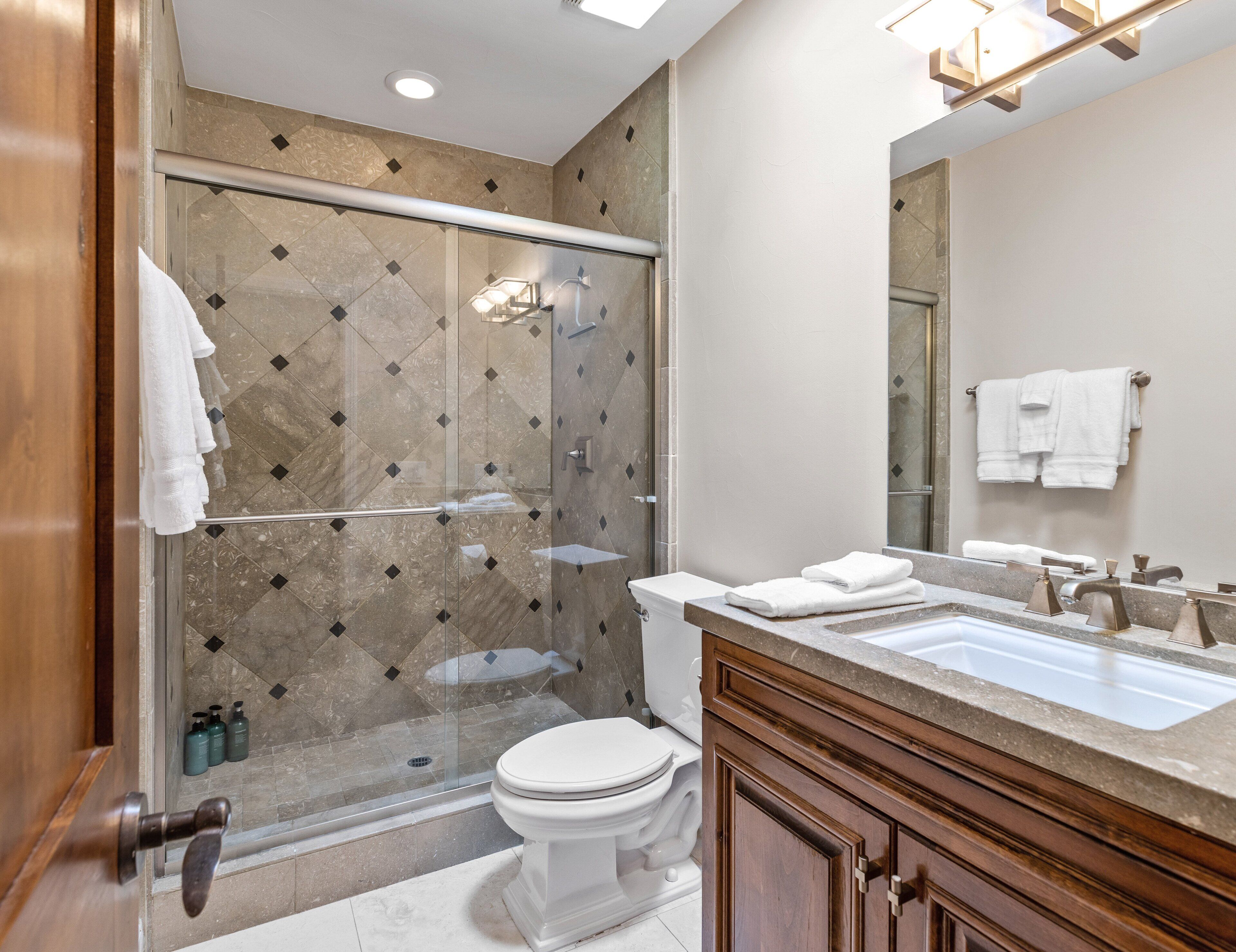 A modern bathroom with a glass-enclosed shower, a white toilet, and a vanity with a mirror.