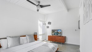 Une chambre à coucher avec un lit, un ventilateur de plafond, une commode, un téléviseur et une fenêtre.
