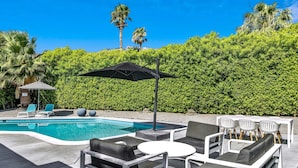 Un espace aménagé au bord de la piscine, avec des chaises longues, une table et un parasol.