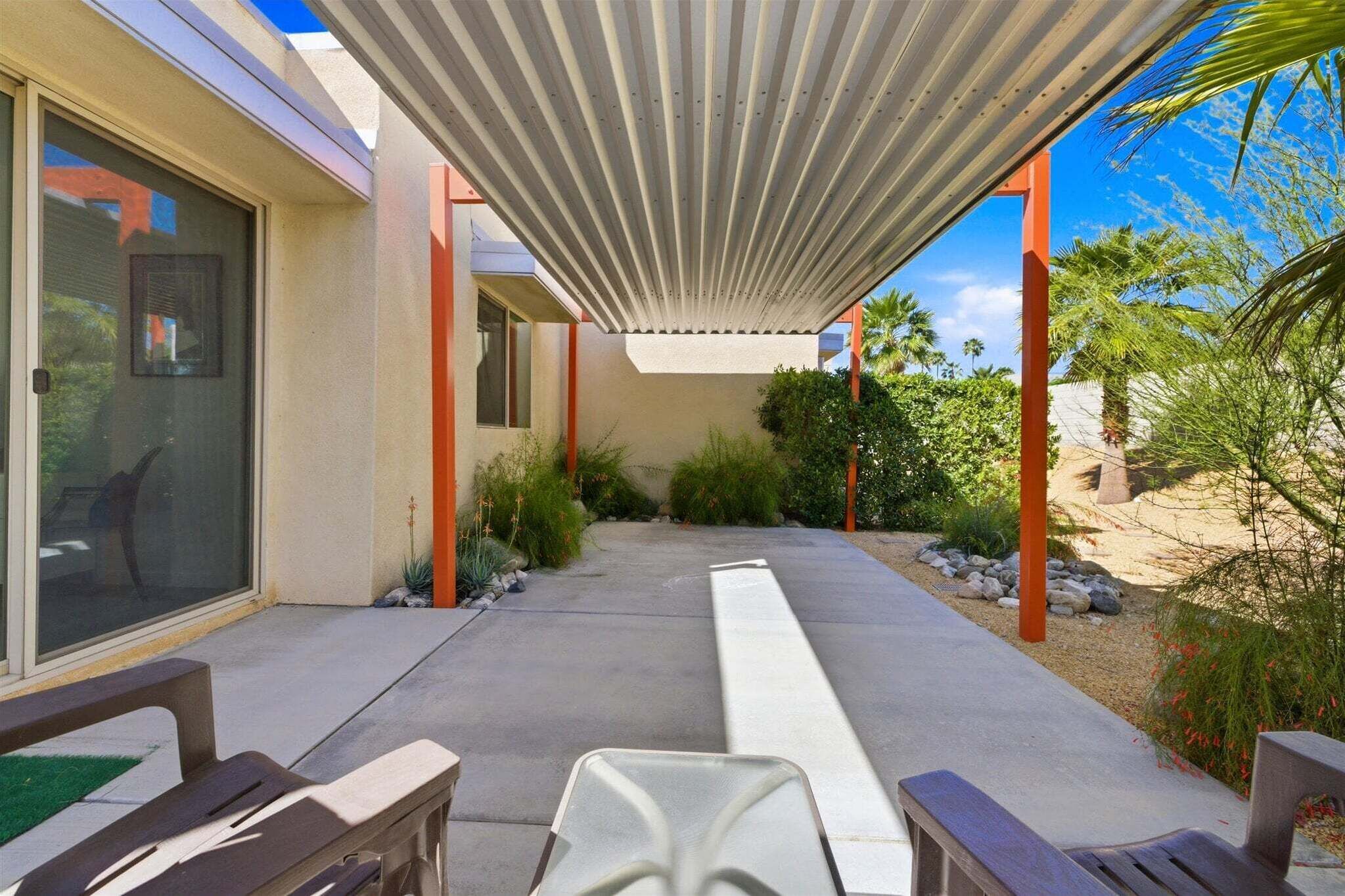 A covered patio with outdoor furniture, a concrete pathway, and a view of a building with large windows and a door.