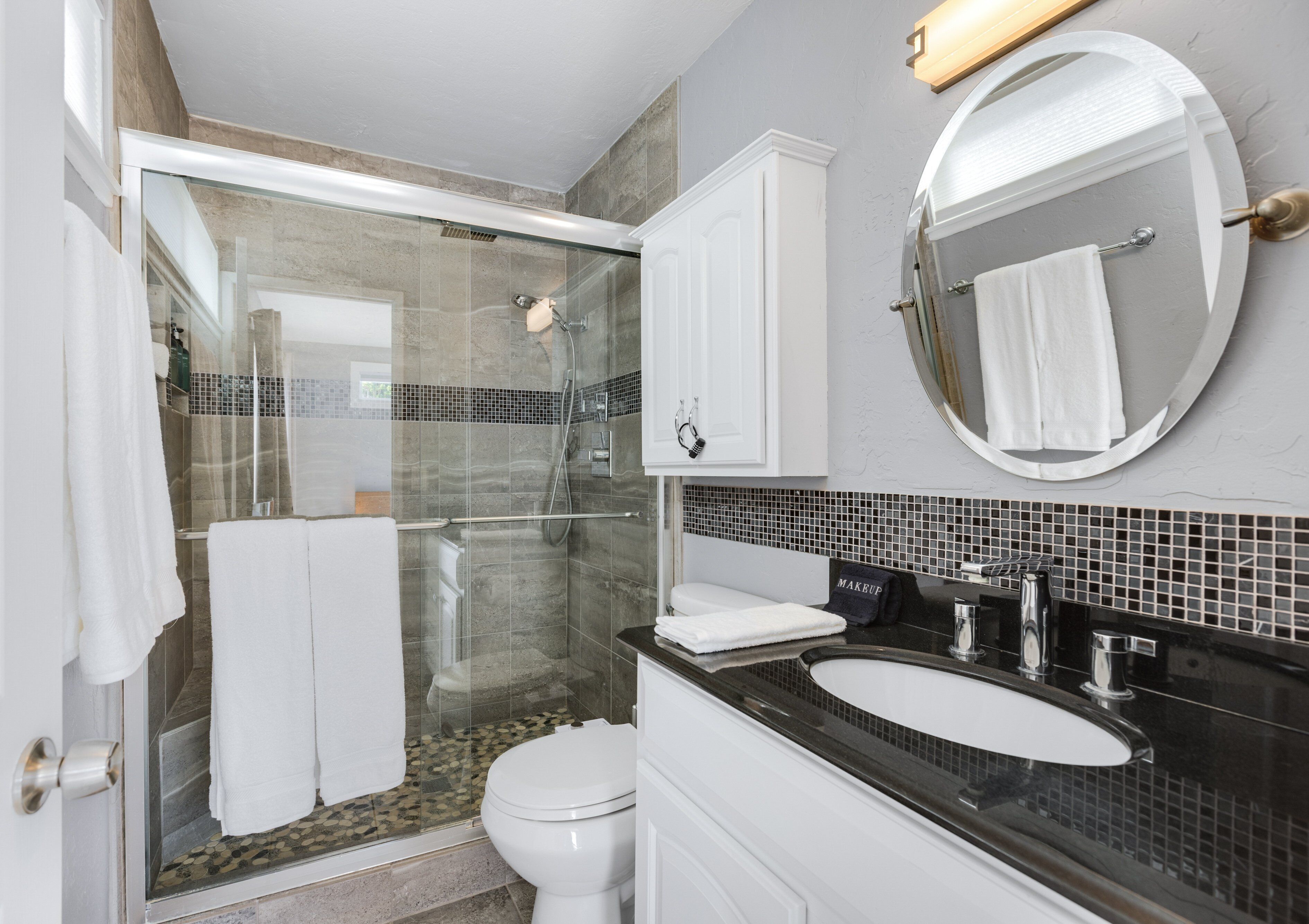 A modern bathroom with a glass-enclosed shower, a white toilet, a vanity with a black countertop, and a large mirror.
