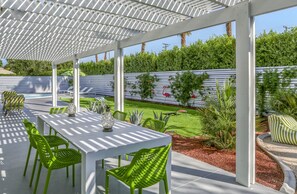 An outdoor patio with a covered seating area, white tables, and green chairs. - Desert Flamingo PS (Palm Springs)