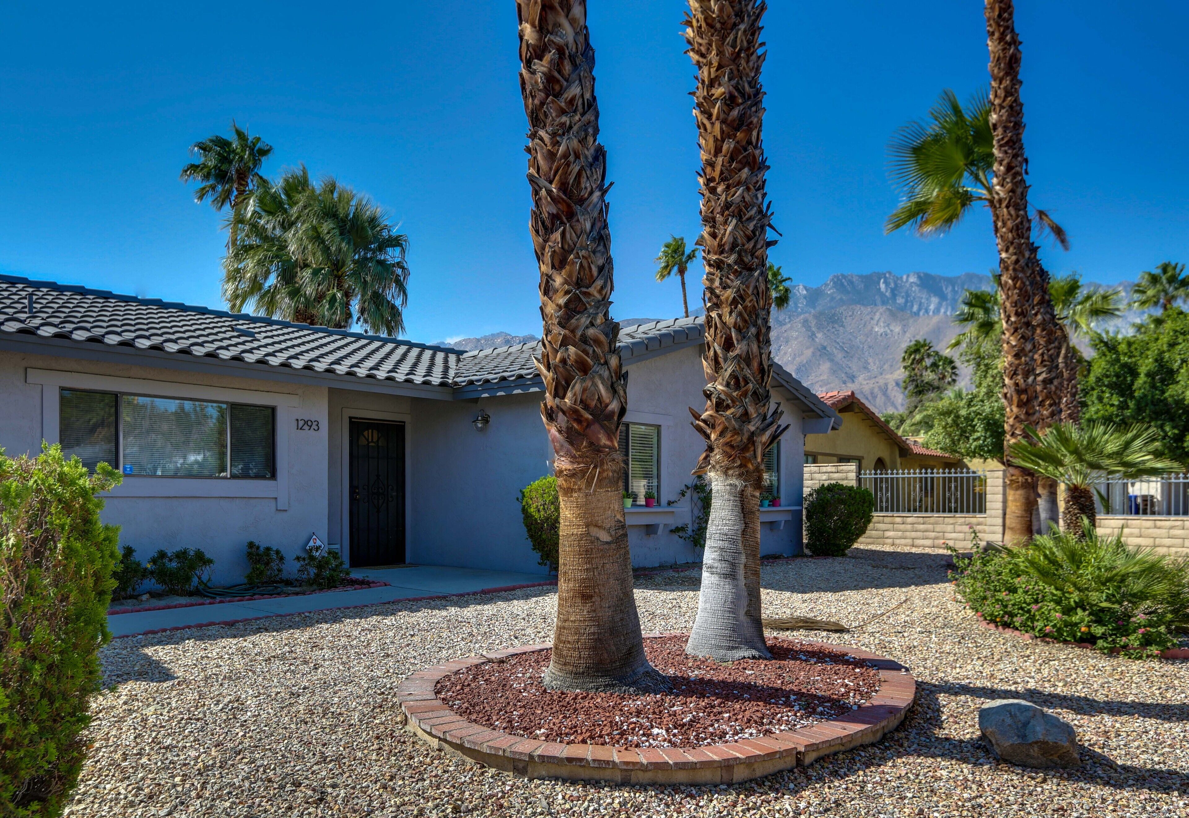 A house with a tiled roof, palm trees, and a mountain in the background.