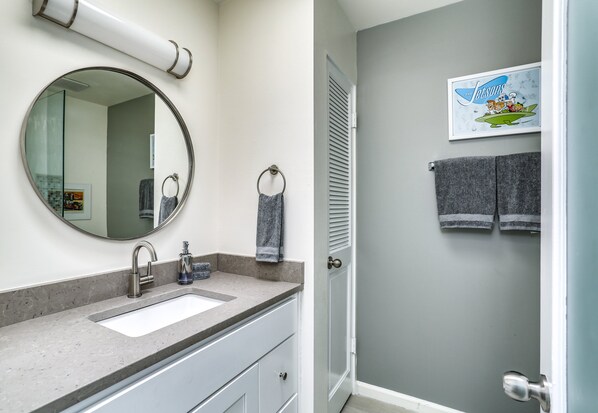 A bathroom with a sink, mirror, towel ring, and a door leading to another room.