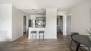 Uma cozinha moderna com eletrodomésticos de aço inoxidável, uma ilha central com banquetas e uma área de jantar com mesa de madeira escura.