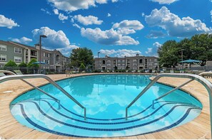 A swimming pool with a tiled deck, surrounded by buildings and trees. - Landing | Modern 2BD, Courtyard, Game Room (Murfreesboro)