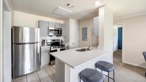 A modern kitchen with stainless steel appliances, a microwave, and a large island with bar stools. - Landing | Chic 1BD, Game Room, Courtyard (Murfreesboro)