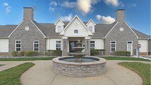 A two-story stone building with a central entrance, a stone fountain, and a well-maintained lawn. - Landing | Chic 1BD, Game Room, Courtyard (Murfreesboro)