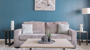 A living room with a grey sofa, two matching pillows, a coffee table with a plant, and a wall-mounted abstract art piece. - Landing | Incredible 1BD, Gym (Houston)