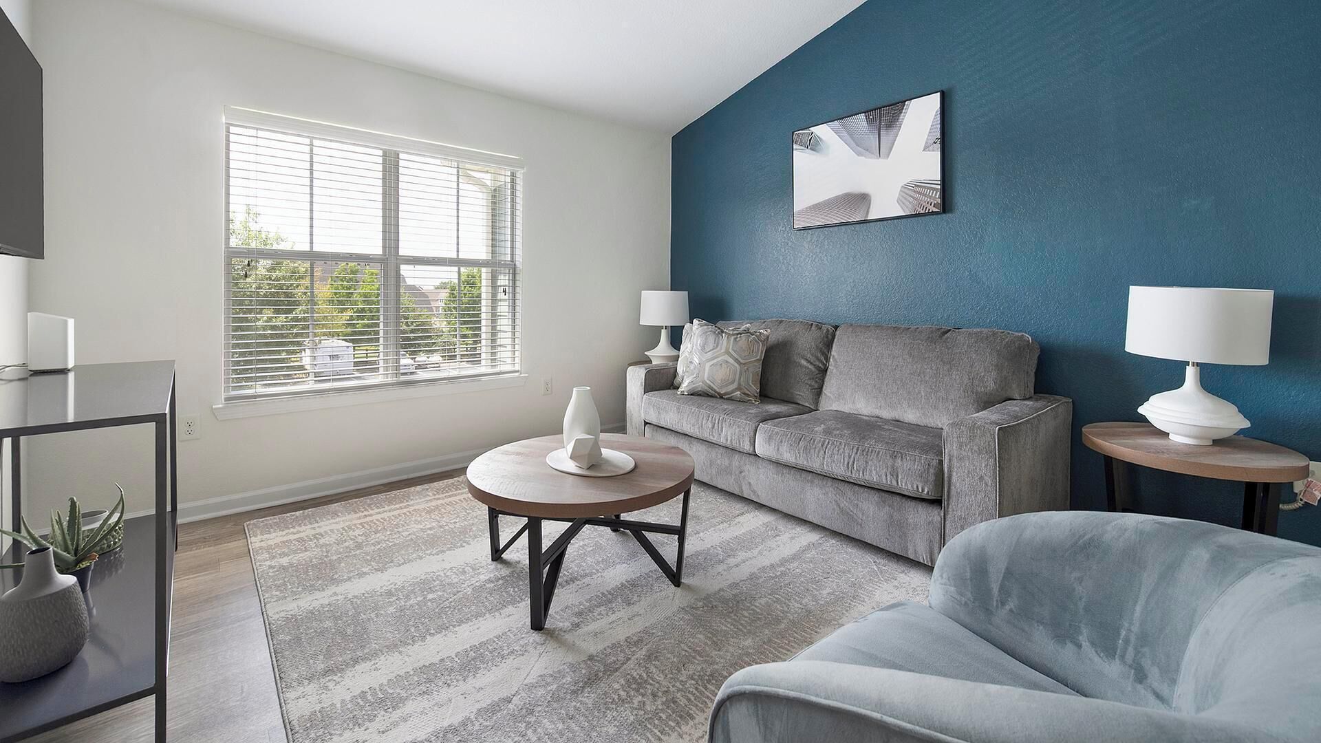 A modern living room with a grey sofa, a round coffee table, and a blue accent wall.