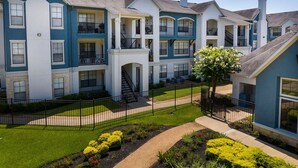 A multi-story residential building with balconies, a central staircase, and a well-maintained lawn. - Landing | Beautiful 2BD, Gym (Houston)
