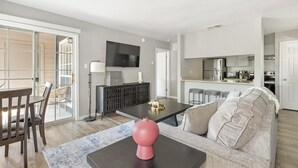 A modern living room with a sofa, a coffee table, and a dining area with chairs. - Landing | Beautiful 1BD, Pool, Clubhouse (San Antonio)
